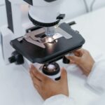 Scientist's hands operating a microscope in a laboratory setting for research purposes.